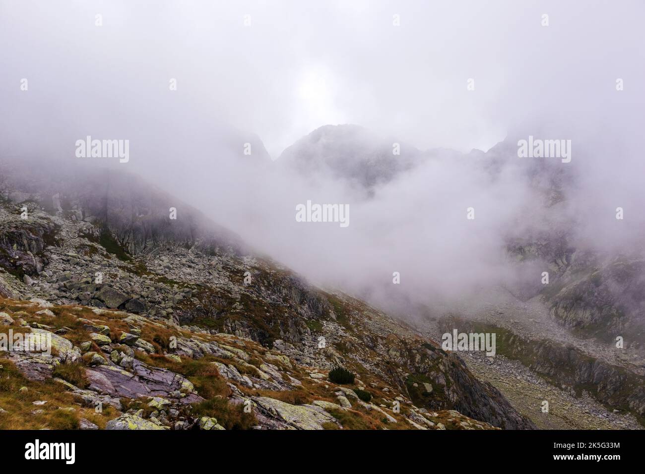 Beeindruckende Landschaft mit großen grau-braunen Bergen in den polnischen Tartaren mit einem felsigen Wanderweg im weißen Nebel und Wolken Stockfoto