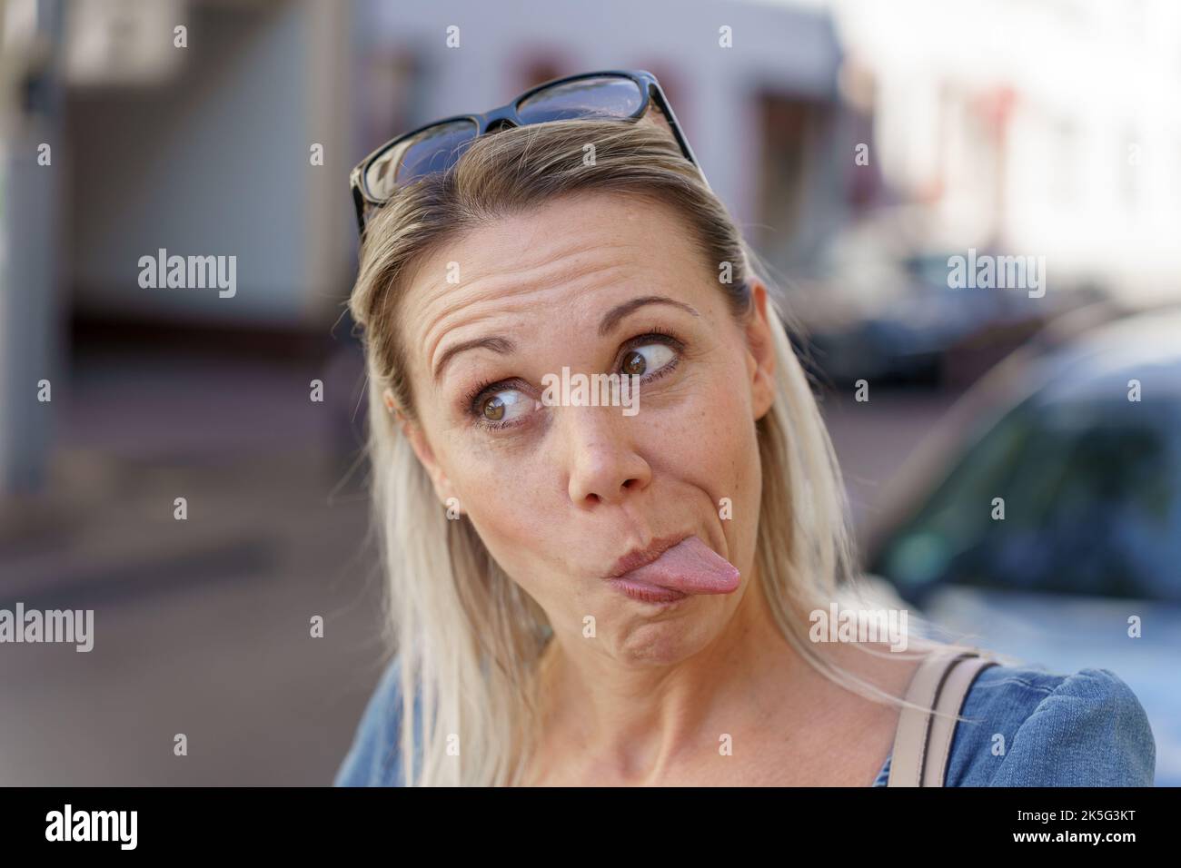 Trendige blonde Frau zieht ein lustiges Gesicht aus ihrer Zunge an der Kamera, als sie wegschaut Stockfoto