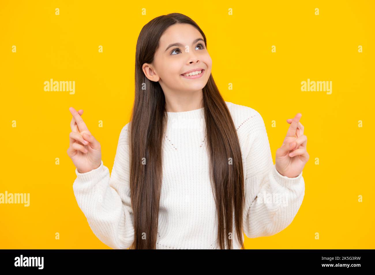 Froh Teenager-Mädchen kreuzt die Finger, erwarten, gute Nachrichten zu hören, isoliert gelben Hintergrund. Glückliches Kind freut sich, dass seine Träume wahr wurden Stockfoto