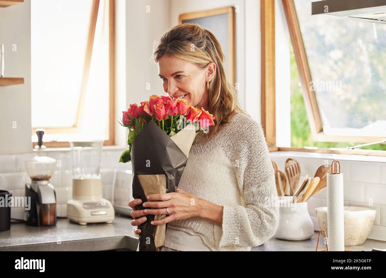 Blumen, Lächeln und eine ältere Frau, die riecht, stiegen in einer Küche, überrascht von einer süßen Geste und einem geheimen Geschenk. Glückliche, romantische und freundliche Überraschung für Stockfoto