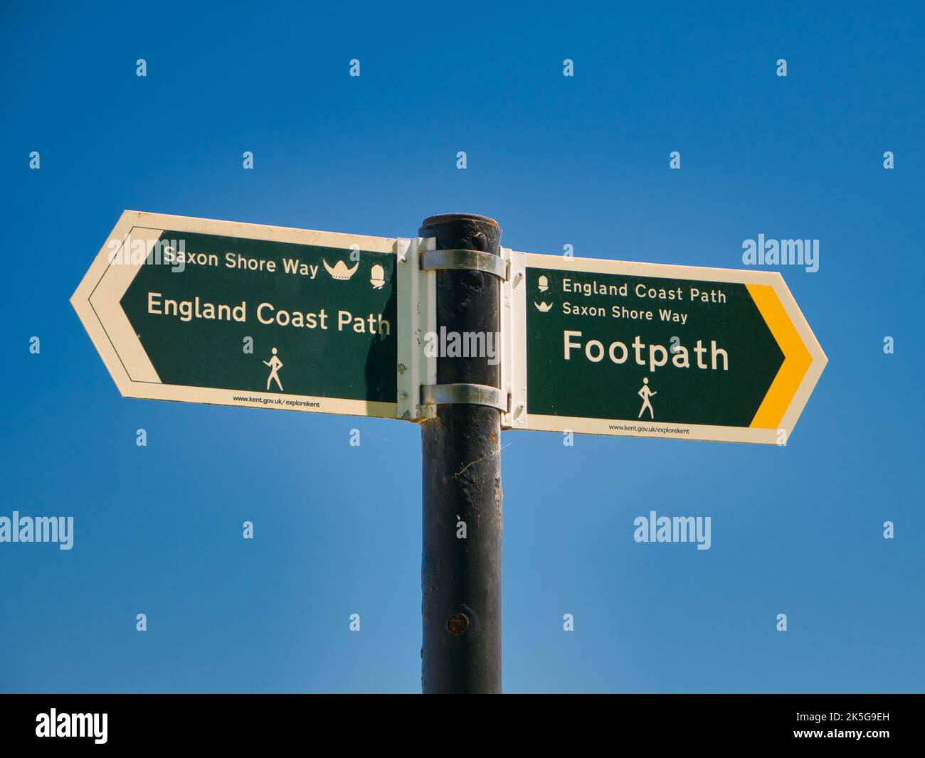 Zwei grüne Schilder auf einem grauen Metallpfosten weisen in die Richtungen des England Coast Path und des Saxon Shore Way. An einem sonnigen Tag im Sommer mit einem klaren, Stockfoto