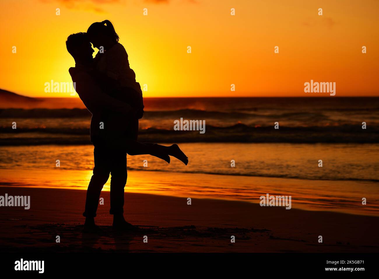 Paar, Strand und Sonnenuntergang mit einem Mann und einer Frau, die sich an der Küste umarmen, mit einem goldenen Blick im Hintergrund. Liebe, Silhouette und Meer mit einem männlichen und Stockfoto