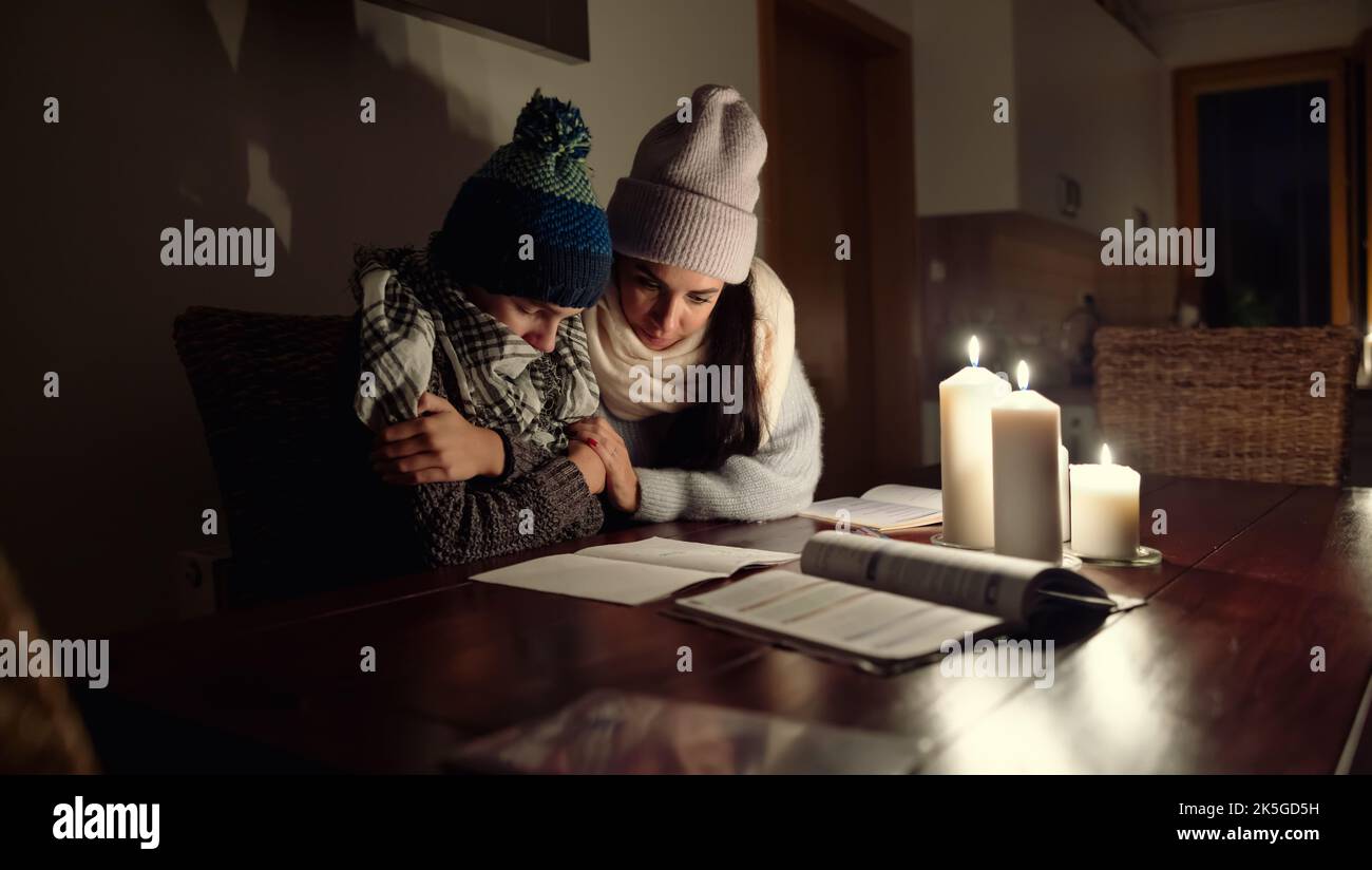 Mutter hält ihren Sohn während eines Balckout aufgrund einer Energiekrise vor Kälte zitternd, während er unter Kerzenlicht studiert. Stockfoto