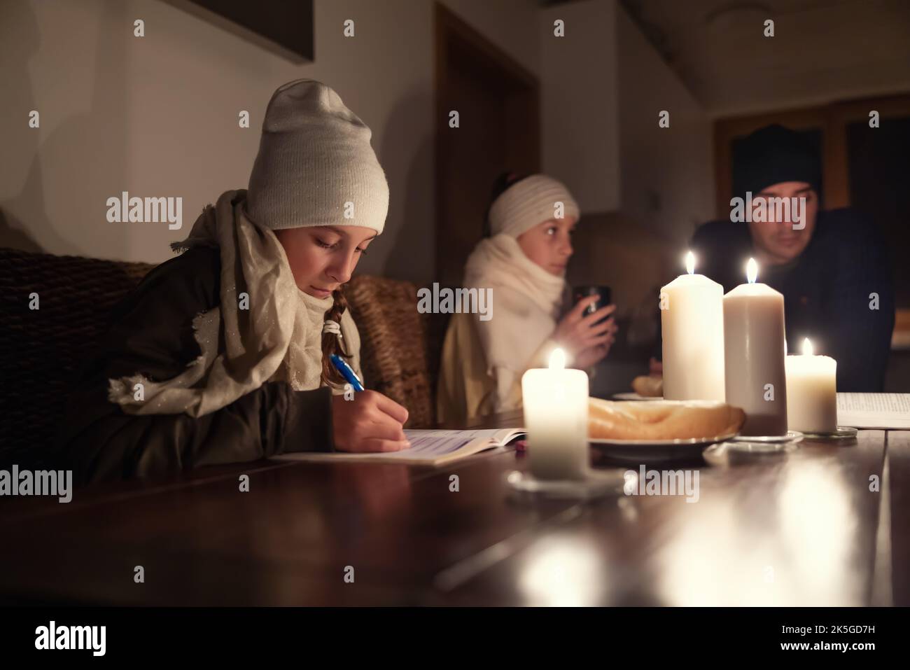 Mädchen im Winterhut und Schal studiert zu Hause am Tisch bei Kerzenlicht, während fanily erlebt Winter Stromausfall. Stockfoto