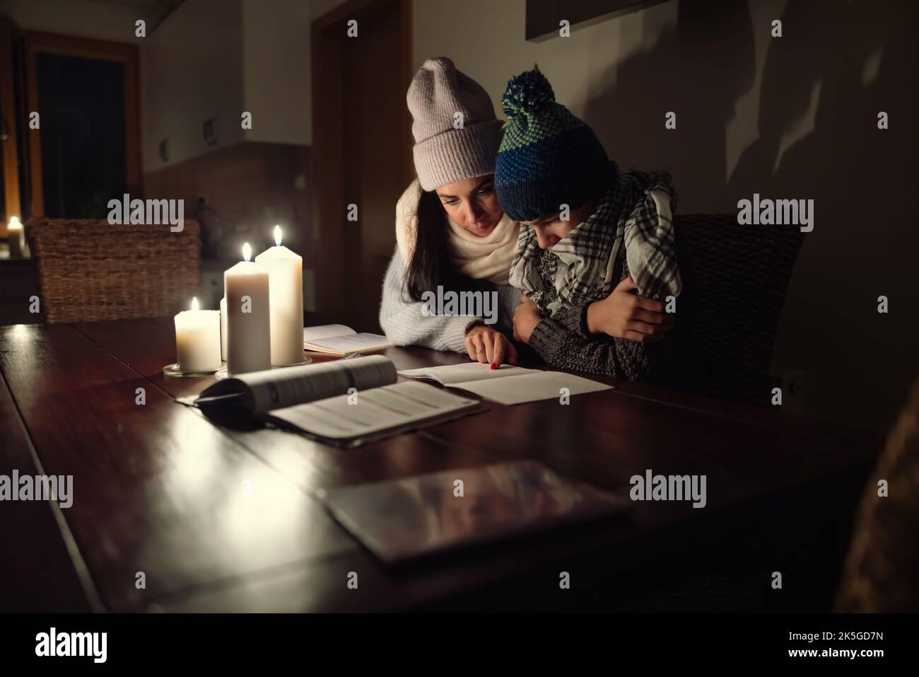 Frau und ihr Sohn sitzen zu Hause in Wintermützen und Schals am Tisch, die im Winter wegen der europäischen Energiekrise vor Kälte zittern. Stockfoto
