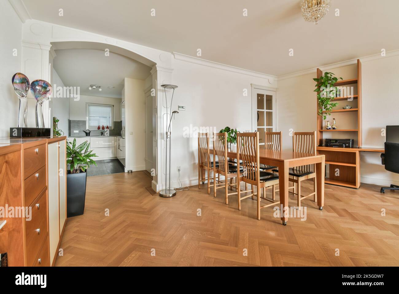Stilvolles Wohndesign der Essecke mit Lampen, die über Holztisch und -Stühlen hängen, in einem modernen Apartment mit großen Fenstern und minimalistischem Design Stockfoto