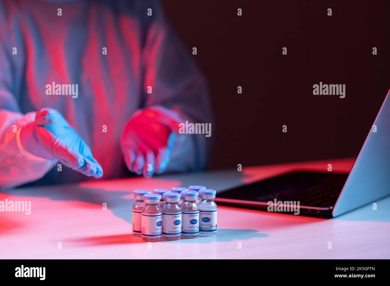 Coronavirus-Impfstoff. Virtuelle Forschung. Medizinische Online-Zusammenarbeit. Wissenschaftlerin in PSA-Handschuhen, die die Dosis der Ampulle auf dem Laptop auf der Videoca aus der Ferne diskutiert Stockfoto