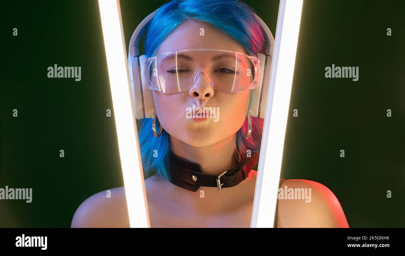 Schlag den Kuss. Futuristisches Mädchen. DJ-Style. Hübsche flirty winkende Frau in Kopfhörer pouts Lippen in LED-Lampe Neonlicht auf schwarzem Hintergrund. Stockfoto