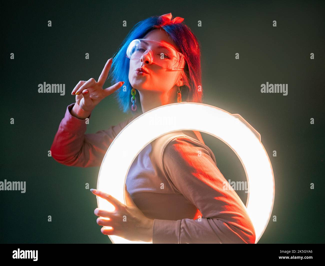 Neonlicht-Modell. Techno-Style. Futuristische Beleuchtung. Flirty nette Frau pouts Lippen mit LED runden Blitz Lampe in rot leuchten isoliert auf dunklen Backgroun Stockfoto