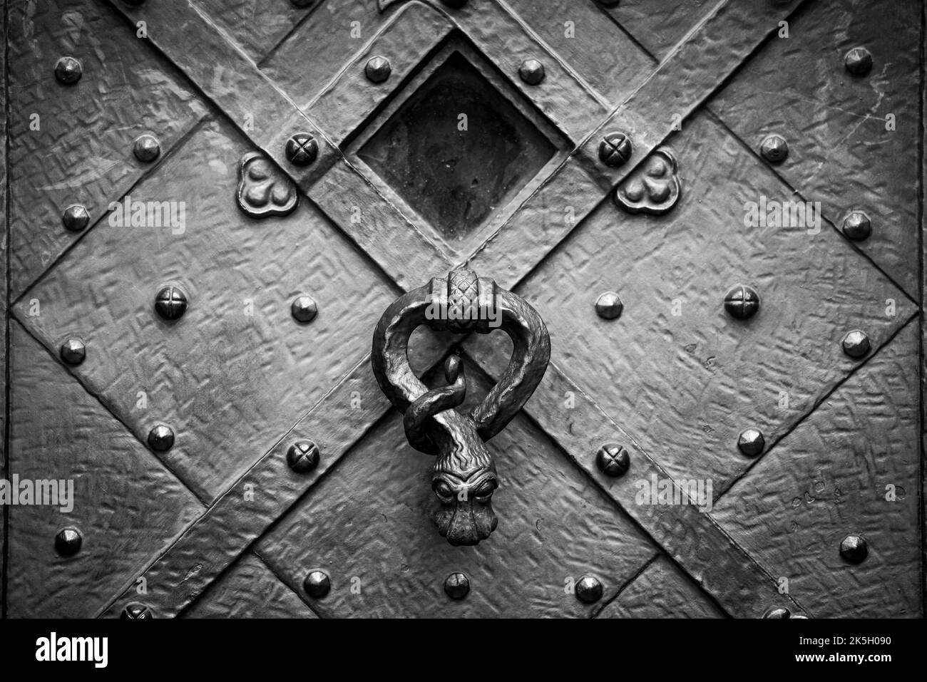 Eine Graustufe eines schlangenförmigen Griffs an einer alten Metalltür Stockfoto