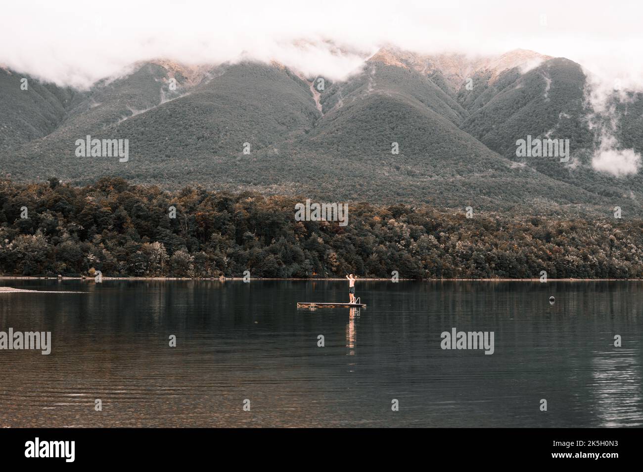 kaukasischer Junge, der in Badehosen gekleidet auf einer kleinen Plattform mit ausgestreckten Armen steht, um in der Mitte des ins Wasser zu springen Stockfoto