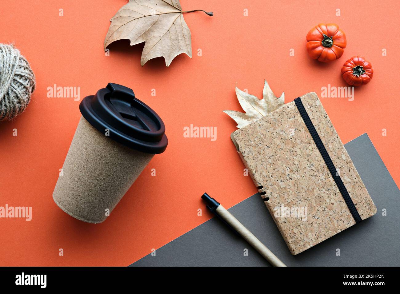 Kaffeebecher mit Naturkorkband. Kaffeebecher zu trockenen Platanenblättern und Deko-Kürbissen. Notizbuch mit passendem Korkbezug. Flach auf orange legen Stockfoto