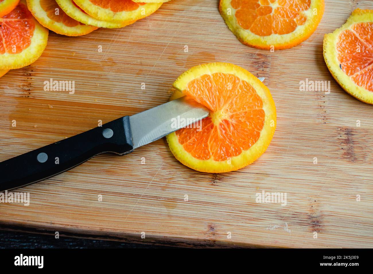 Dünn geschnittene Cara Cara Orange mit einem Trennmesser: Dünn geschnittene Orange auf einem Bambus-Schneidebrett mit einem Küchenmesser Stockfoto