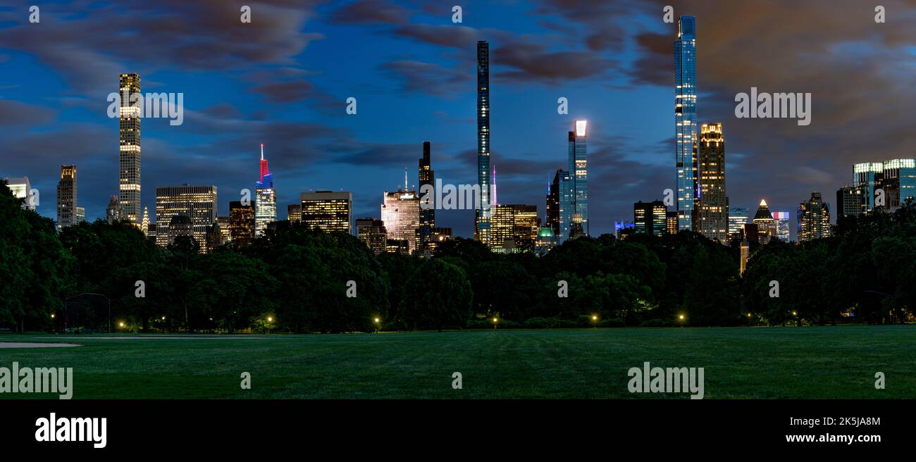 Skyline von Midtown Manhattan bei Nacht vom Central Park Panorama mit Rasen im Vordergrund. Stockfoto