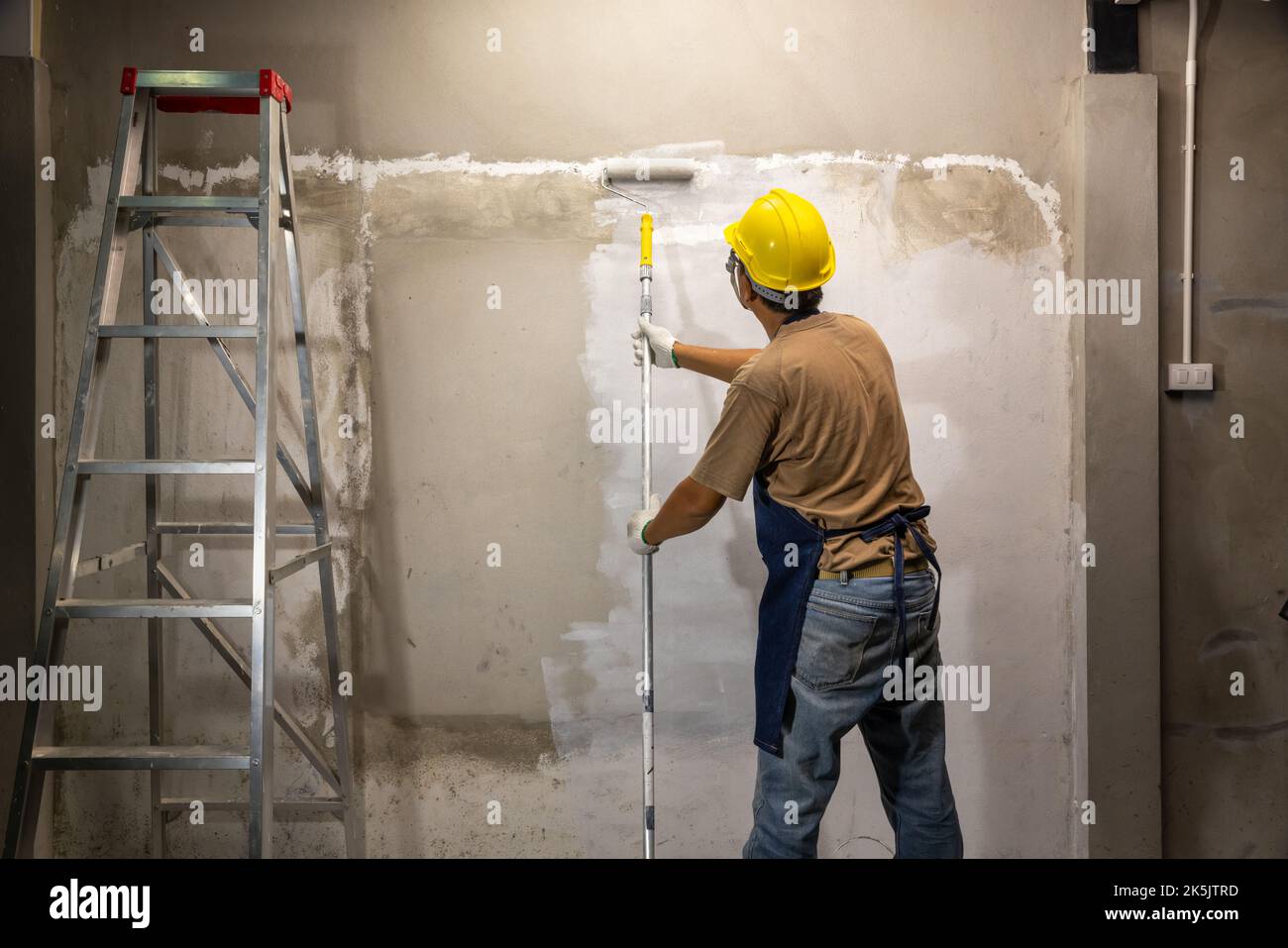 Grundierung auf Ölbasis auf alte Betonwand vor dem Auftragen der Hauptfarbe auffüllen. Renovierungskonzept Stockfoto