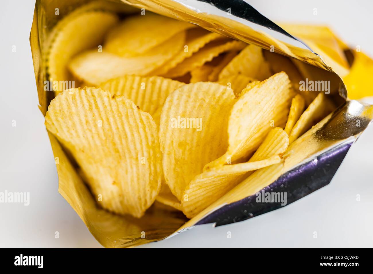 Ansicht von trockenen knusprigen frittierten Wellkartoffelchips in offener Tüte auf weißem Hintergrund, selektiver Fokus. Stockfoto