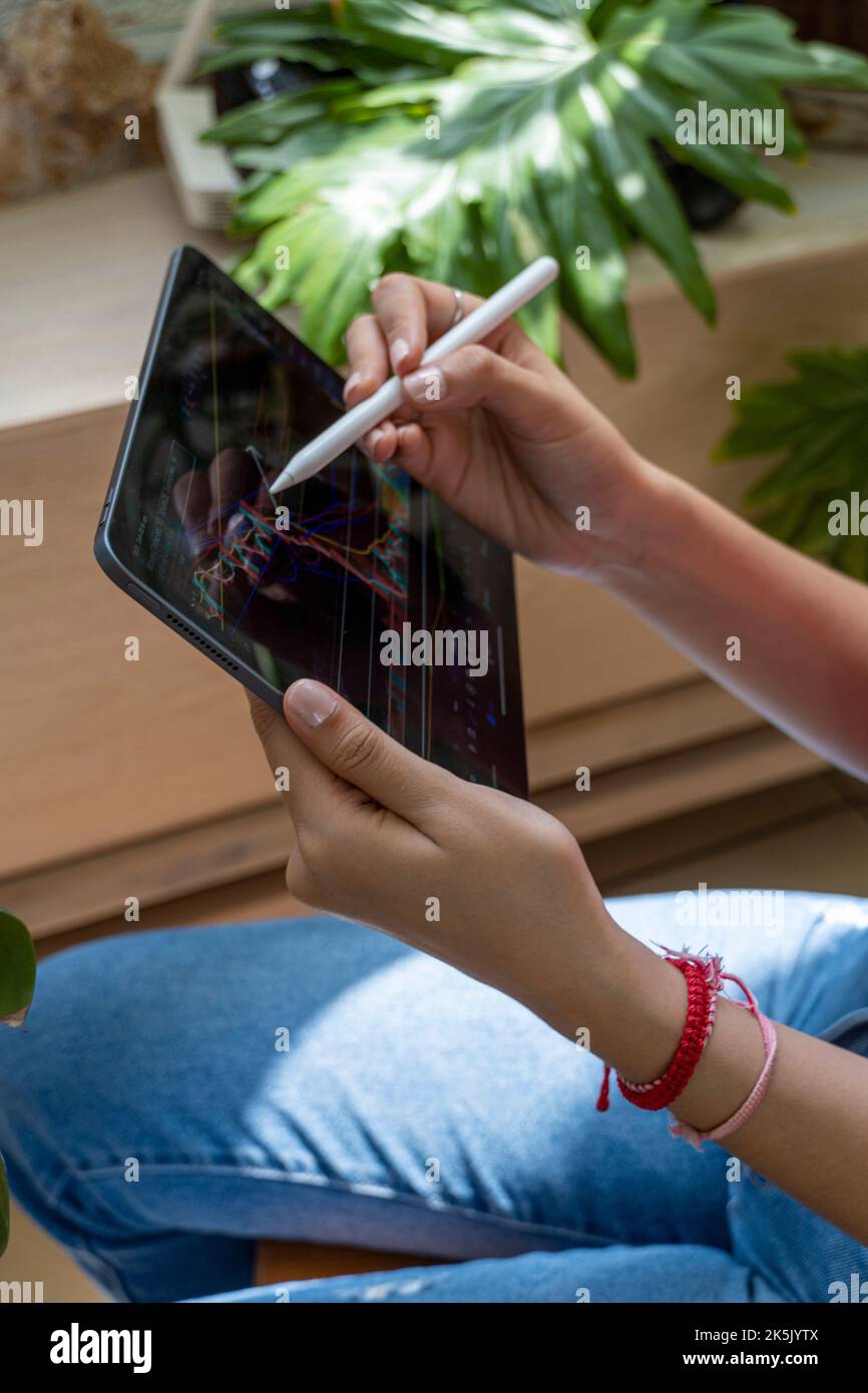 Junge Frau, die den Aktienmarkt auf ihrem Tablet beobachtet, während sie auf dem Chart zeichnet Stockfoto