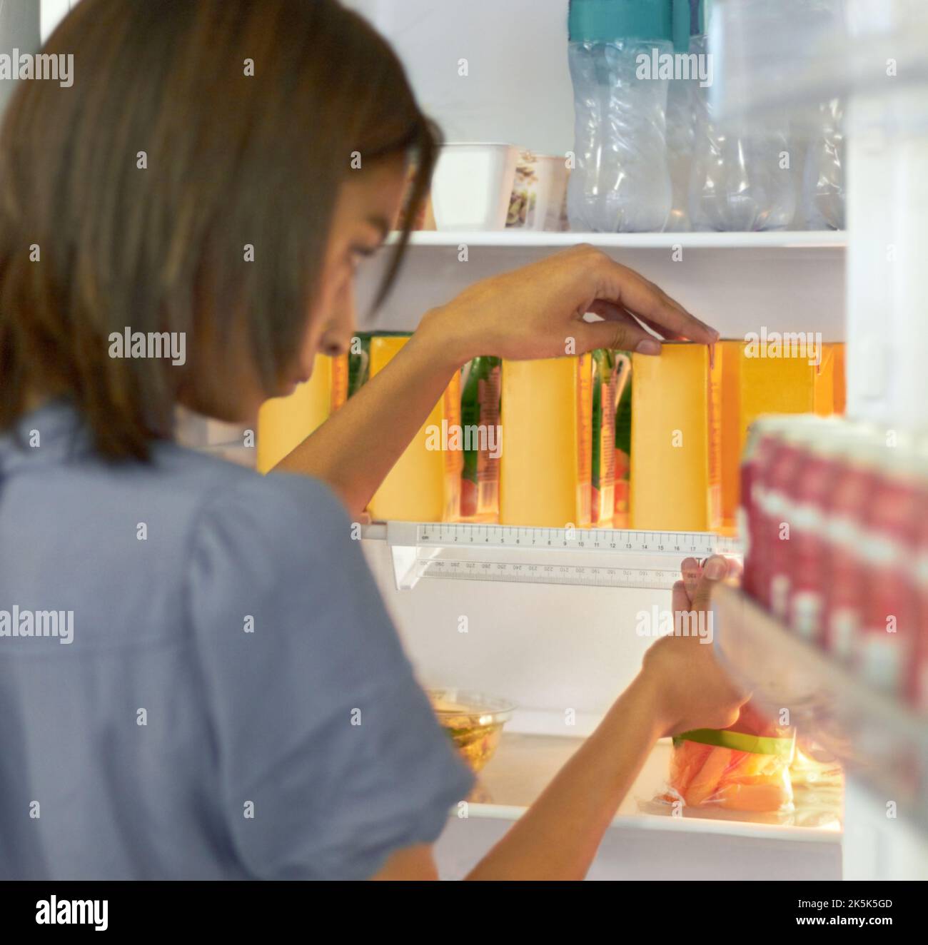 Probleme mit OCD. Junge Frau, die den Inhalt ihres Kühlschranks sorgfältig organisiert. Stockfoto