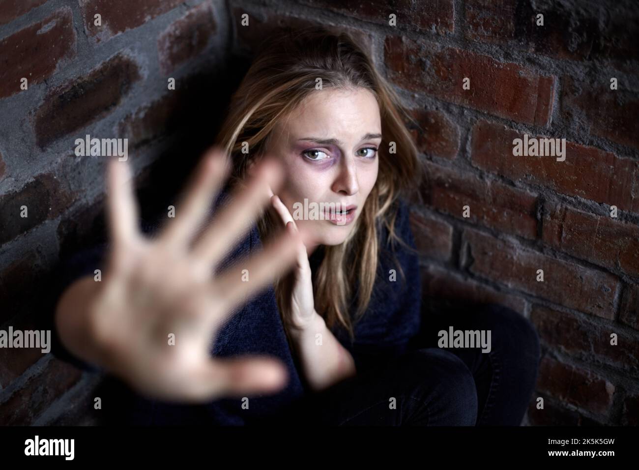 Bitte nicht. Missbrauchte junge Frau, die sich in einer Ecke kauerte und in einer Stoppgeste ausstreute. Stockfoto