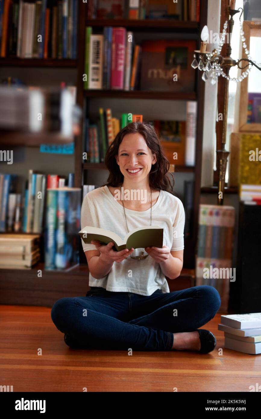 Zu viele Bücher und so wenig Zeit. Porträt einer jungen Frau, die mit gekreuzten Beinen auf dem Boden einer Buchhandlung sitzt und liest. Stockfoto