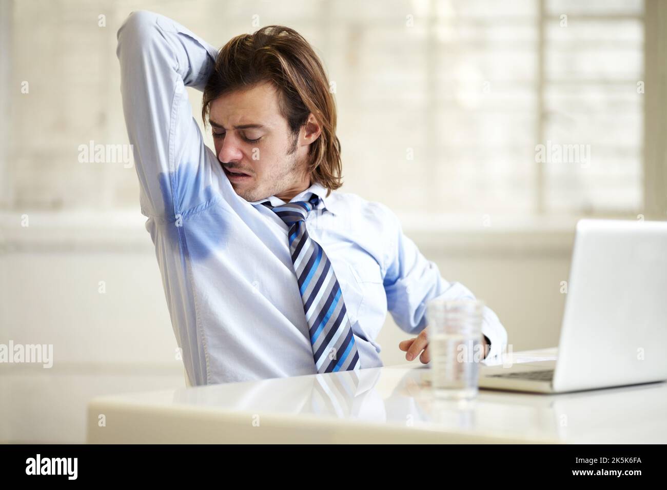 Äh, wie ist das passiert. Ein junger Geschäftsmann überprüft seine verschwitzten Achselhöhlen bei der Arbeit. Stockfoto