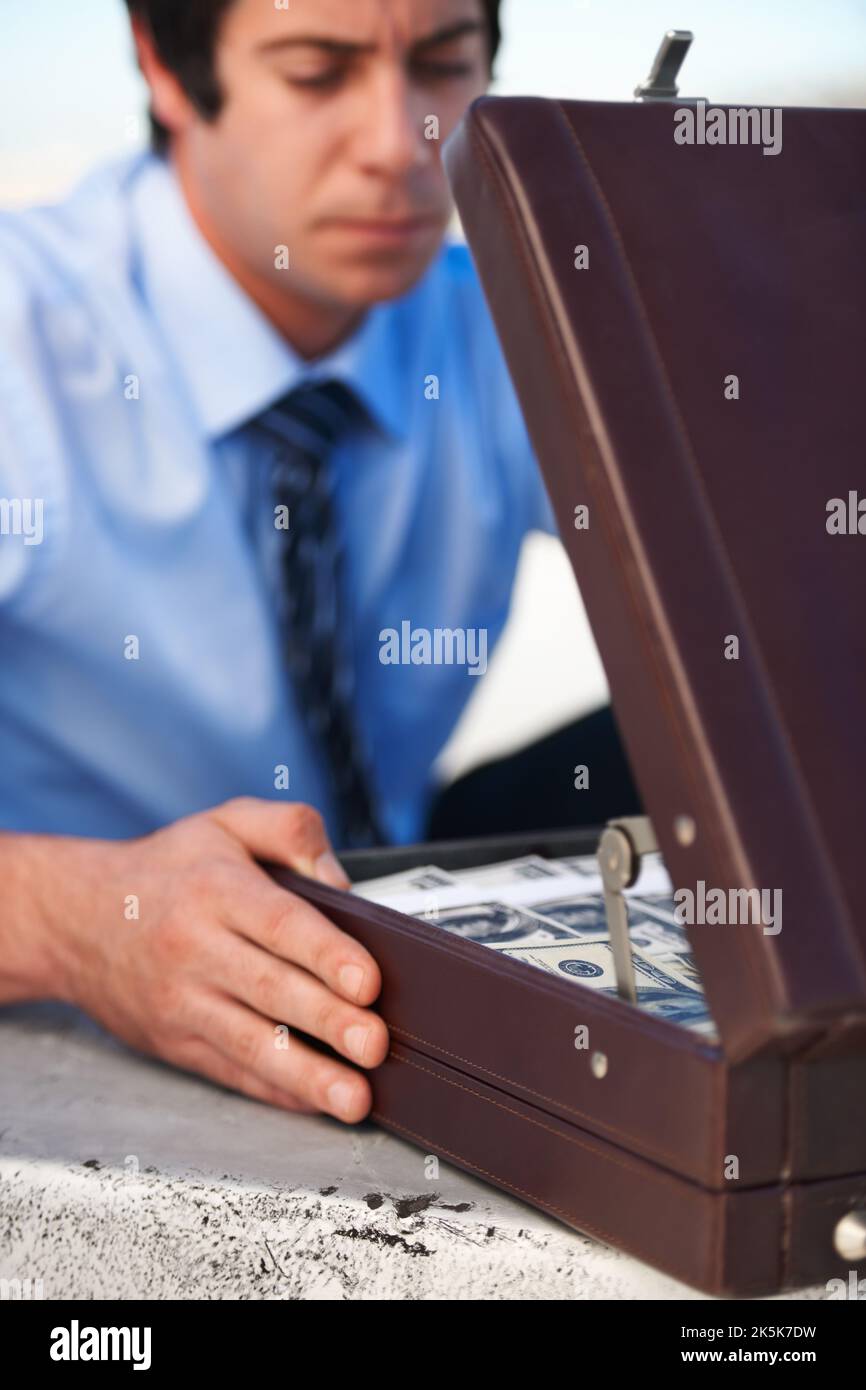 Eine schwierige Entscheidung treffen. Ein Mann aus dem Unternehmen, der in seine Aktentasche schaut, in der Geld und eine Waffe enthalten sind. Stockfoto