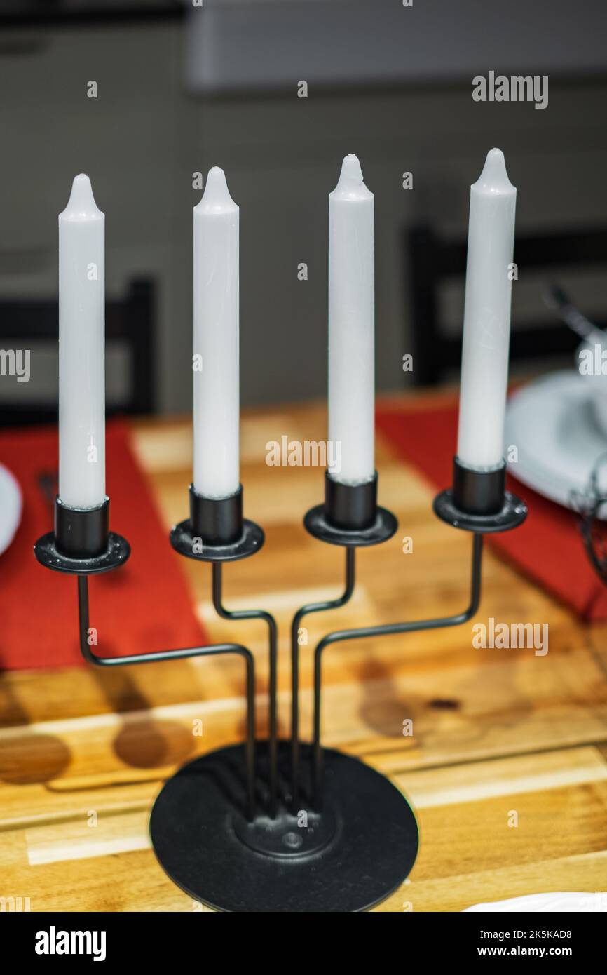 Kerzenleuchter, Kerzenhalter, schwarz, Metall auf einem Holztisch. Kerzenständer mit vier weißen Kerzen. Eiserner Kerzenleuchter. Niemand Stockfoto