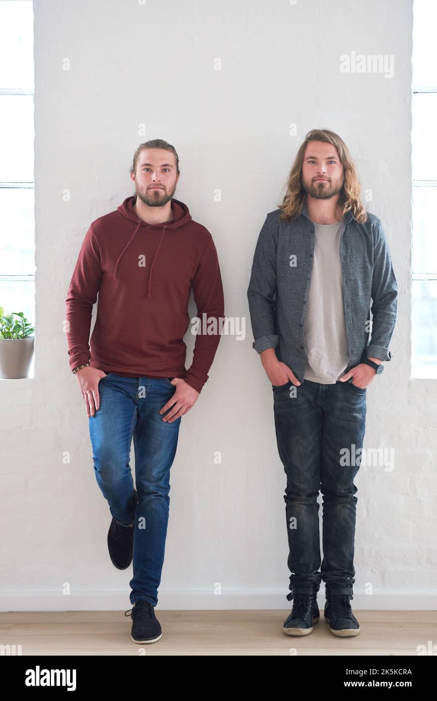 Portrait von Zwillingsbrüdern, die im Studio an einer Wand stehen. Junge Zwillinge, Geschwister und Familie junger Männer nebeneinander. Beziehung zum Bruder Stockfoto