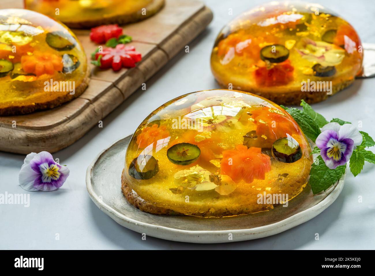 Zitronengelee-Globen mit frischem Obst, essbaren Blumen und Goldflocken auf Pistazien-Keks - Gourmet-Dessert Stockfoto Zitronengelee-Globen mit frischem Obst, essbaren Blumen und Goldflocken auf Pistazien-Keks - Gourmet-Dessert Stockfoto
