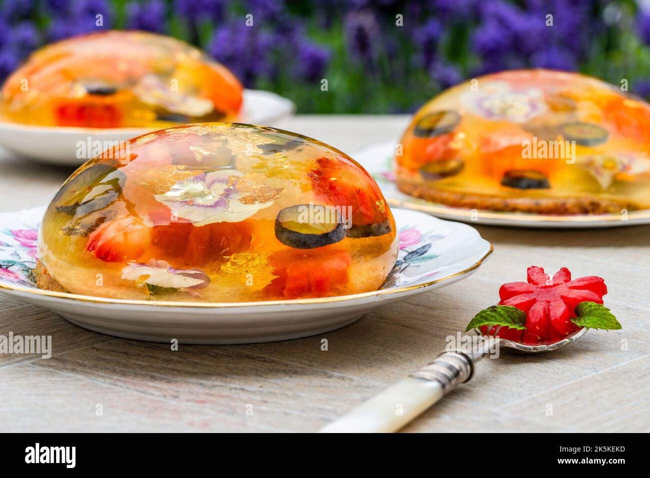 Zitronengelee-Globen mit frischem Obst, essbaren Blumen und Goldflocken auf Pistazien-Keks - Gourmet-Dessert Stockfoto Zitronengelee-Globen mit frischem Obst, essbaren Blumen und Goldflocken auf Pistazien-Keks - Gourmet-Dessert Stockfoto
