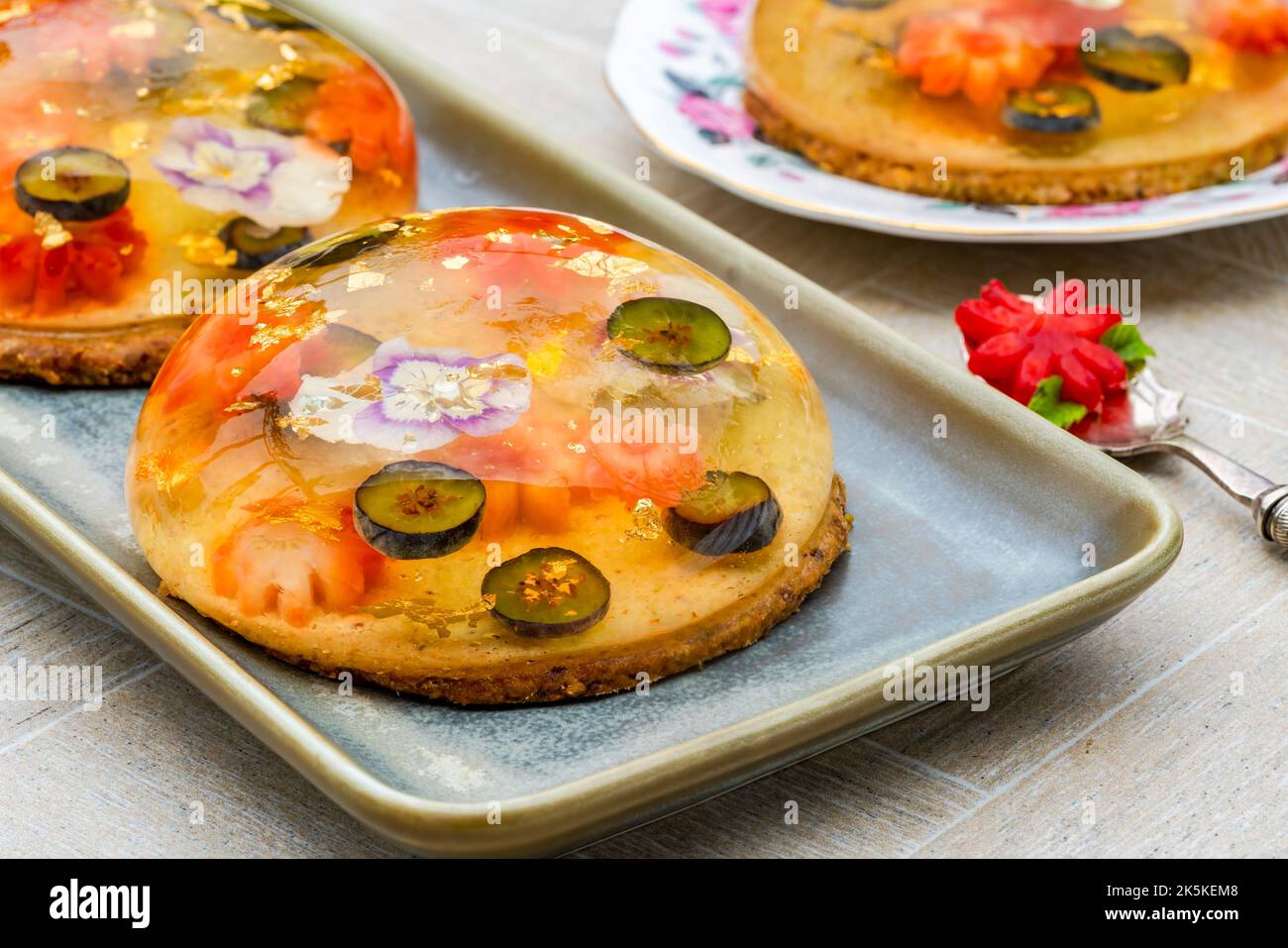 Zitronengelee-Globen mit frischem Obst, essbaren Blumen und Goldflocken auf Pistazien-Keks - Gourmet-Dessert Stockfoto Zitronengelee-Globen mit frischem Obst, essbaren Blumen und Goldflocken auf Pistazien-Keks - Gourmet-Dessert Stockfoto