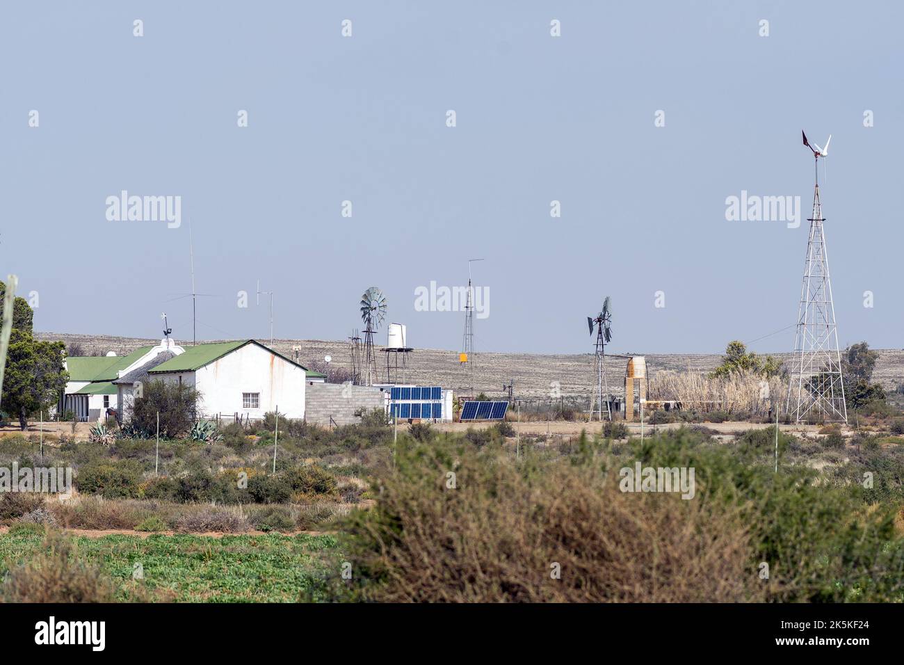 LOXTON, SÜDAFRIKA - SEP 2, 2022: Solar- und Windkraft-Erzeugung auf einem Bauernhof in der Nähe von Loxton im nördlichen Kap Karoo. Ein Haus und Windmühlen sind sichtbar Stockfoto