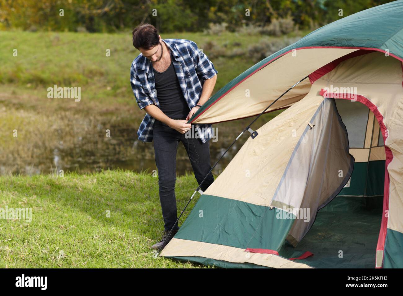 Sein Zelt mit dem letzten Schliff ausgestattet. Junger Mann, der im Freien ein Zelt aufstellt. Stockfoto