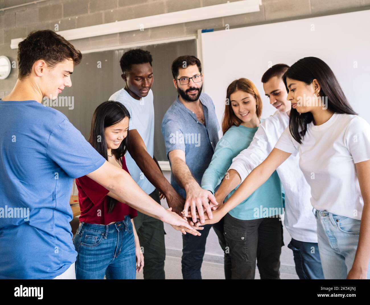 Gruppe multiethnischer Teenager, die sich mit dem Lehrer als Symbol für Zusammenarbeit und Teamarbeit die Hände schütteln Stockfoto