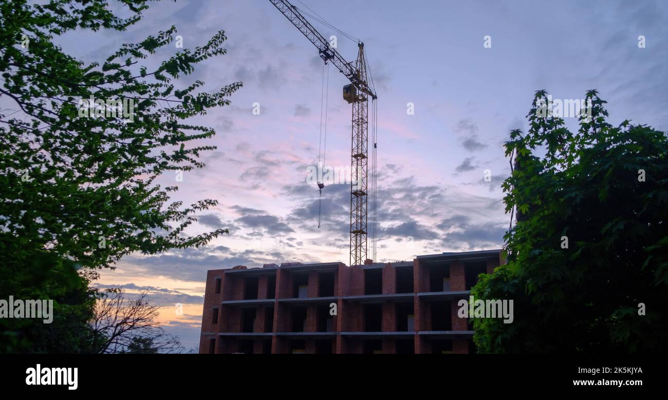 Baukran auf dem Hintergrund des Himmels. Baustelle. Industriebaukrane und Gebäudesilhouetten über der Sonne bei Sonnenaufgang. Downl Stockfoto