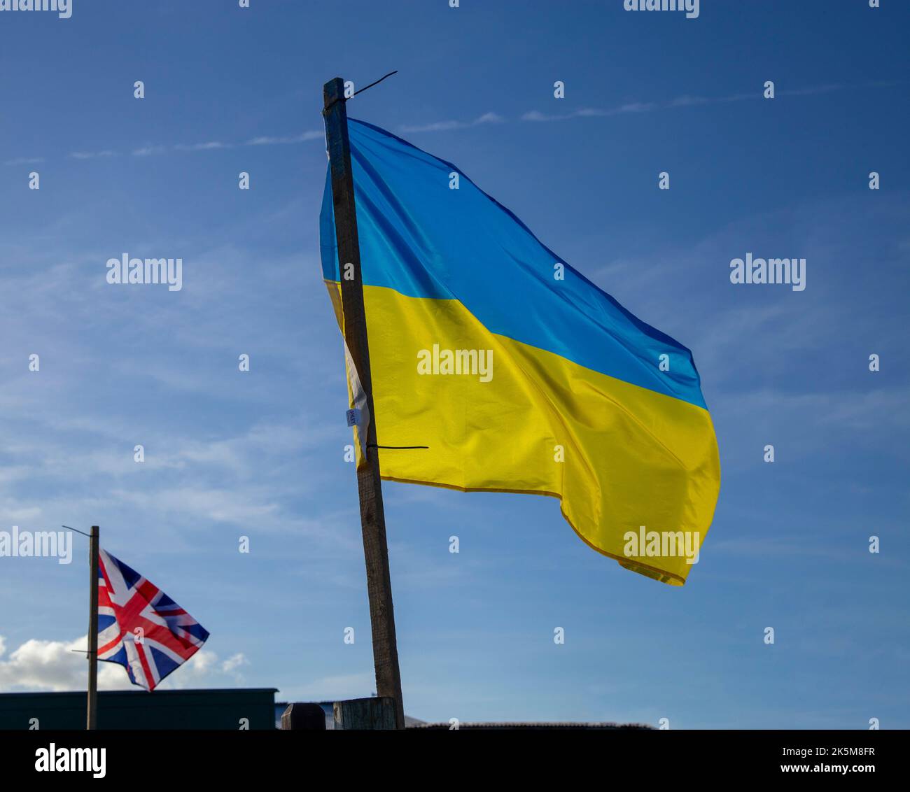 Ukrainische Flagge mit einer Union Jack-Flagge neben einem klaren blauen Himmel. Stockfoto
