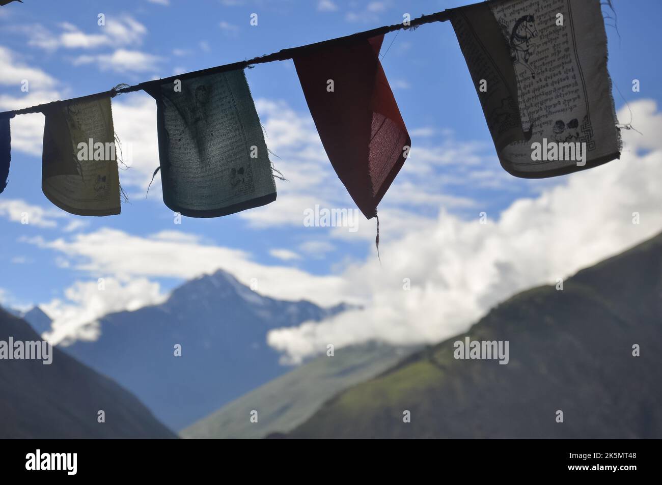 Bunte tibetische Flaggen mit Schriftzug vor dem Hintergrund von Bergen und Wolken Stockfoto