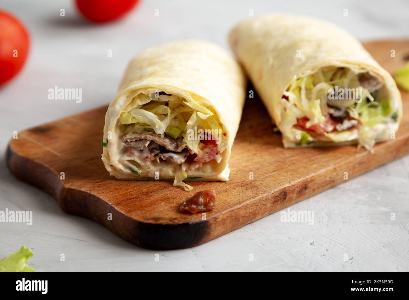 Hausgemachter BLT Tomate Salat Speck Wrap mit Mayo auf einem Holzbrett auf einem grauen Hintergrund, Seitenansicht. Stockfoto