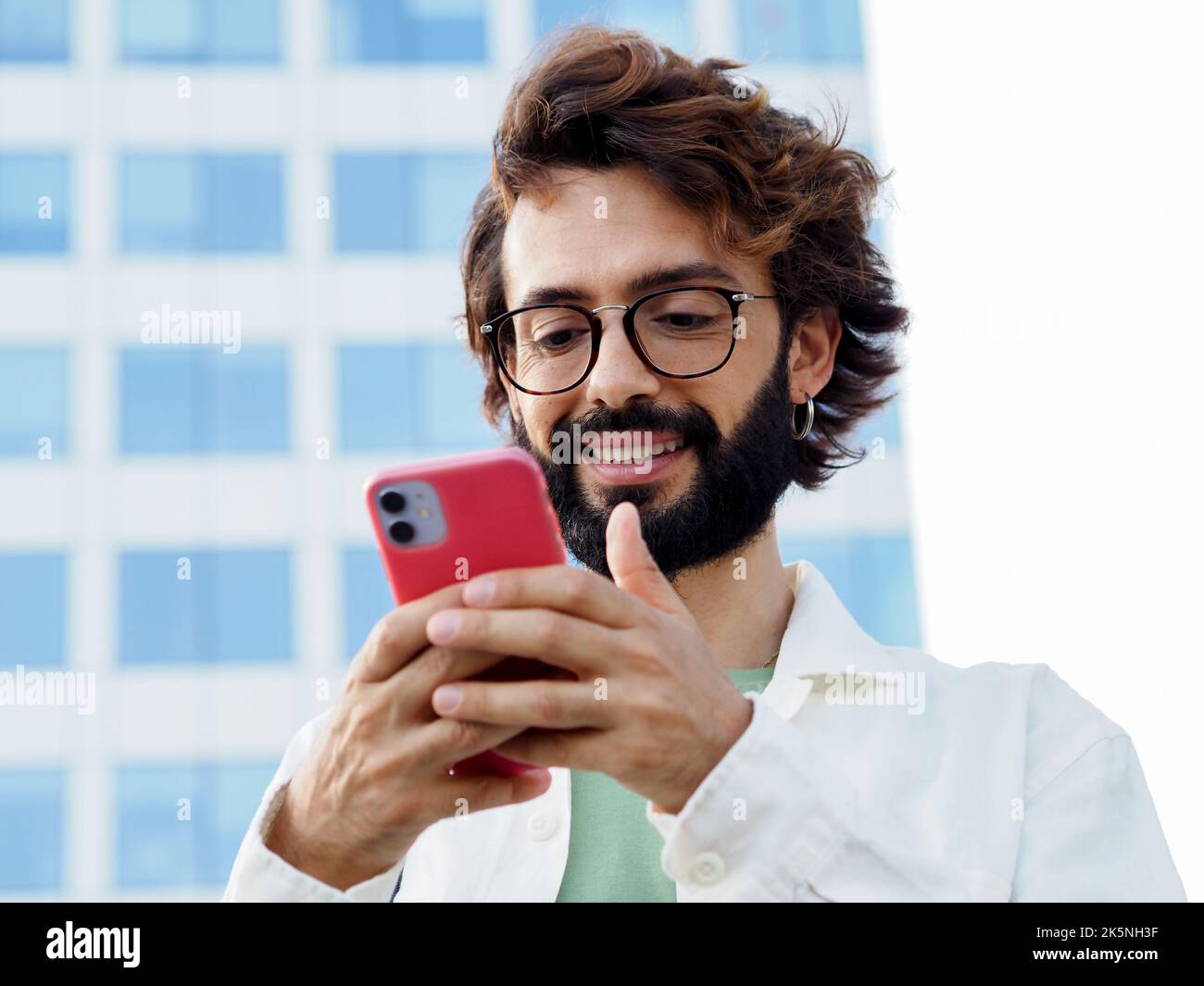Ein junger, lächelnder italienischer Mann, der mit einem Mobiltelefon in einer Stadt chattet Stockfoto