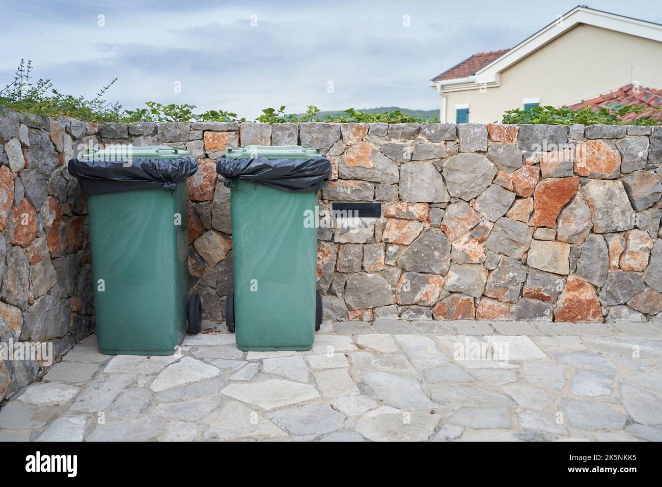 Grüne Mülltonnen neben der Steinmauer. Stockfoto