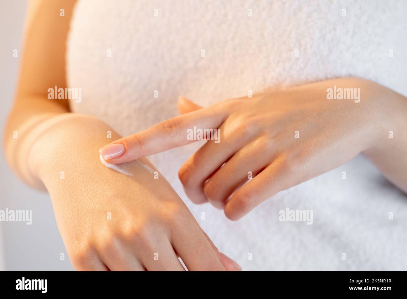 Körperpflege. Schönheit der Handhaut. Geschmeidig pflegend. Unkenntlich Frau mit Handtuch auftragen Creme auf Arm in hellem Hintergrund. Stockfoto