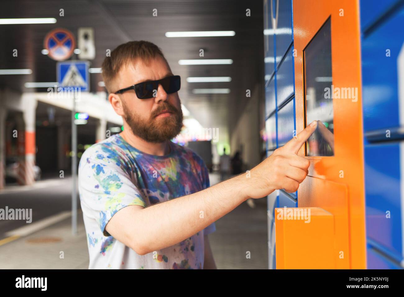 Der Mann gibt den Paketcode auf dem Bildschirm ein und holt das Paket vom automatischen Postautomaten ab. Mann hält Smartphone über automatische Self-Service-Mail-Terminal cl Stockfoto