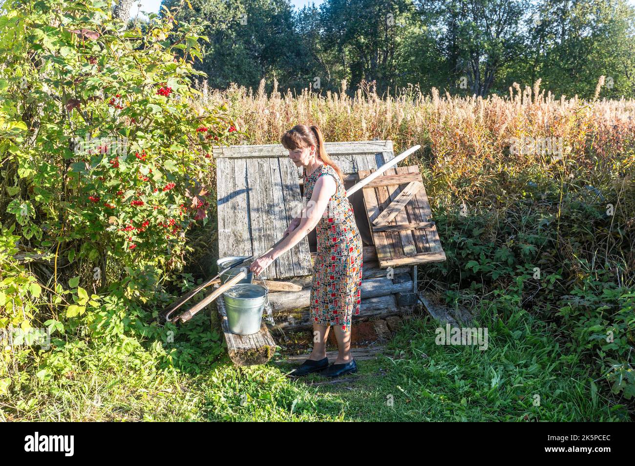 Borovichi, Russland - 13. September 2022: Junge attraktive Frau in der Nähe des Dorfes hölzernen Brunnen im Sommer sonnigen Tag Stockfoto