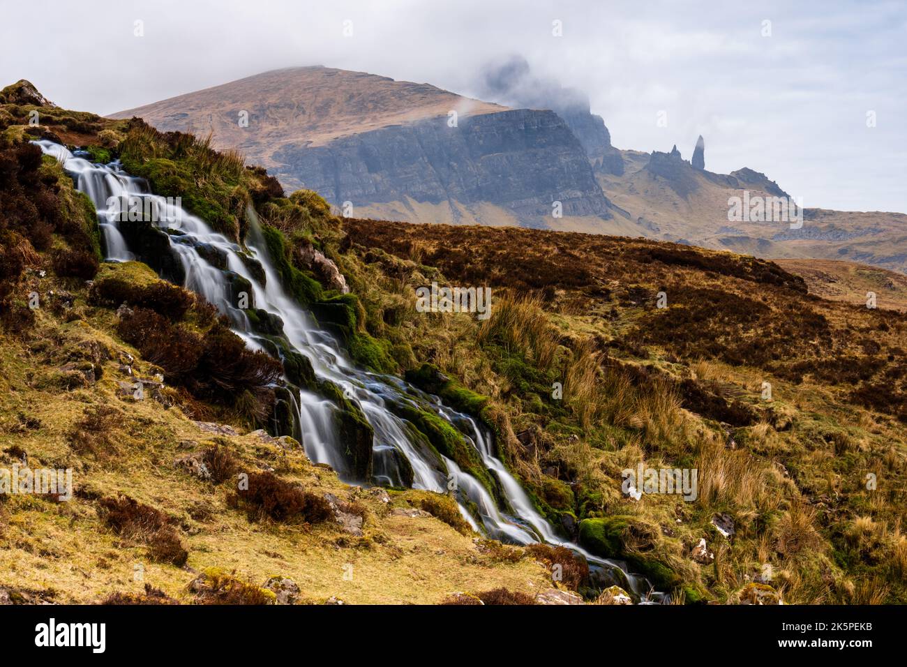Ein wunderschöner Wasserfall, der die mit Moos bedeckten Felsen mit nebligen Bergen in der Ferne hinunterfließt Stockfoto