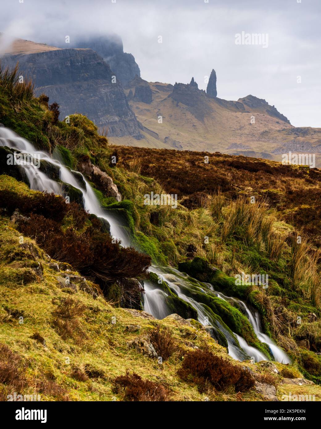 Ein wunderschöner Wasserfall, der die mit Moos bedeckten Felsen mit nebligen Bergen in der Ferne hinunterfließt Stockfoto