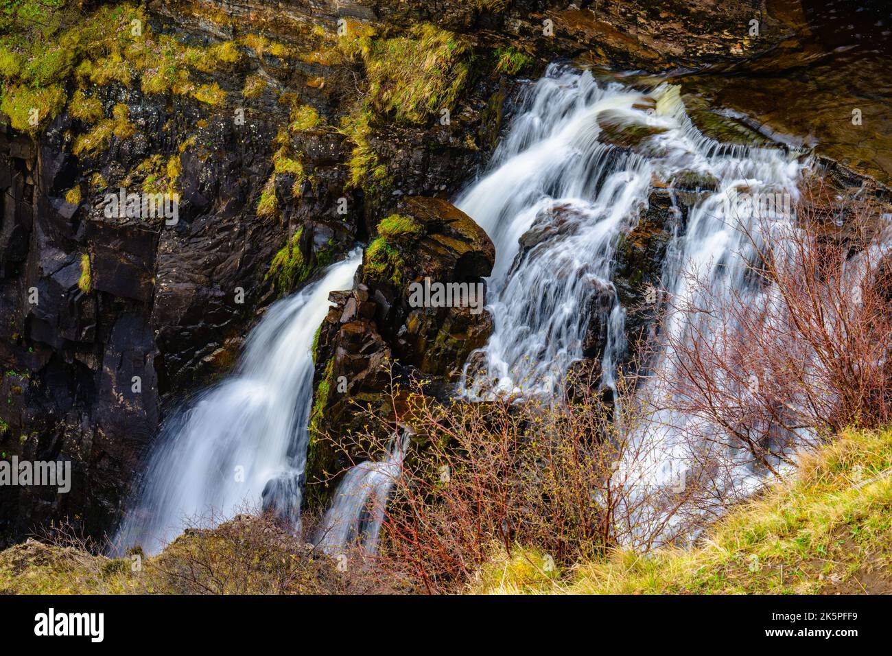 Ein wunderschöner Wasserfall, der die mit Moos bedeckten Felsen hinunter fließt und von blattlosen Bäumen umgeben ist Stockfoto