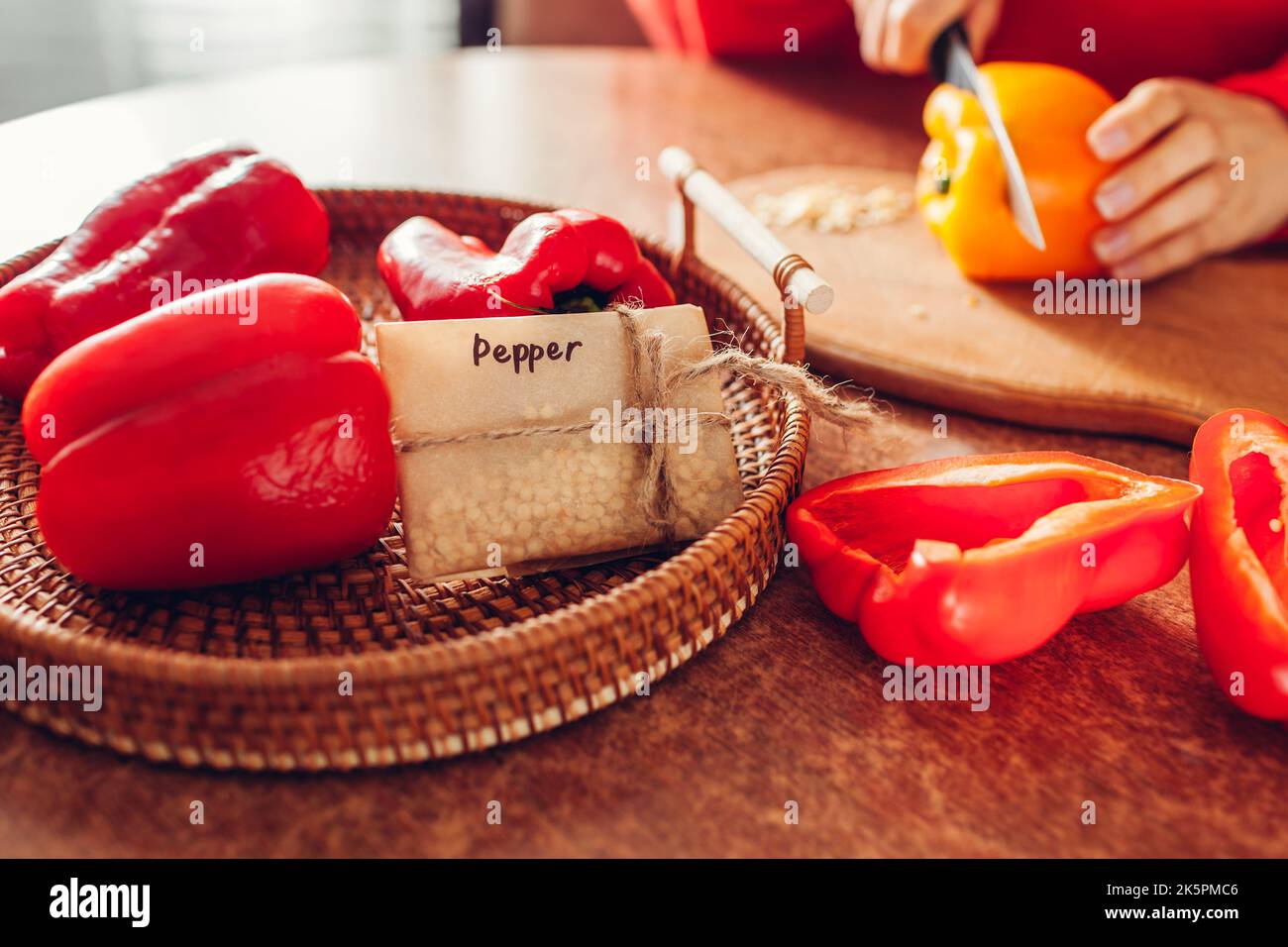 Nahaufnahme der Papierverpackung mit gesammelten Samen von Paprika auf Tablett zu Hause. Schneiden von Gemüse, um Samen von roten gelben Paprika zu pflücken. Stockfoto