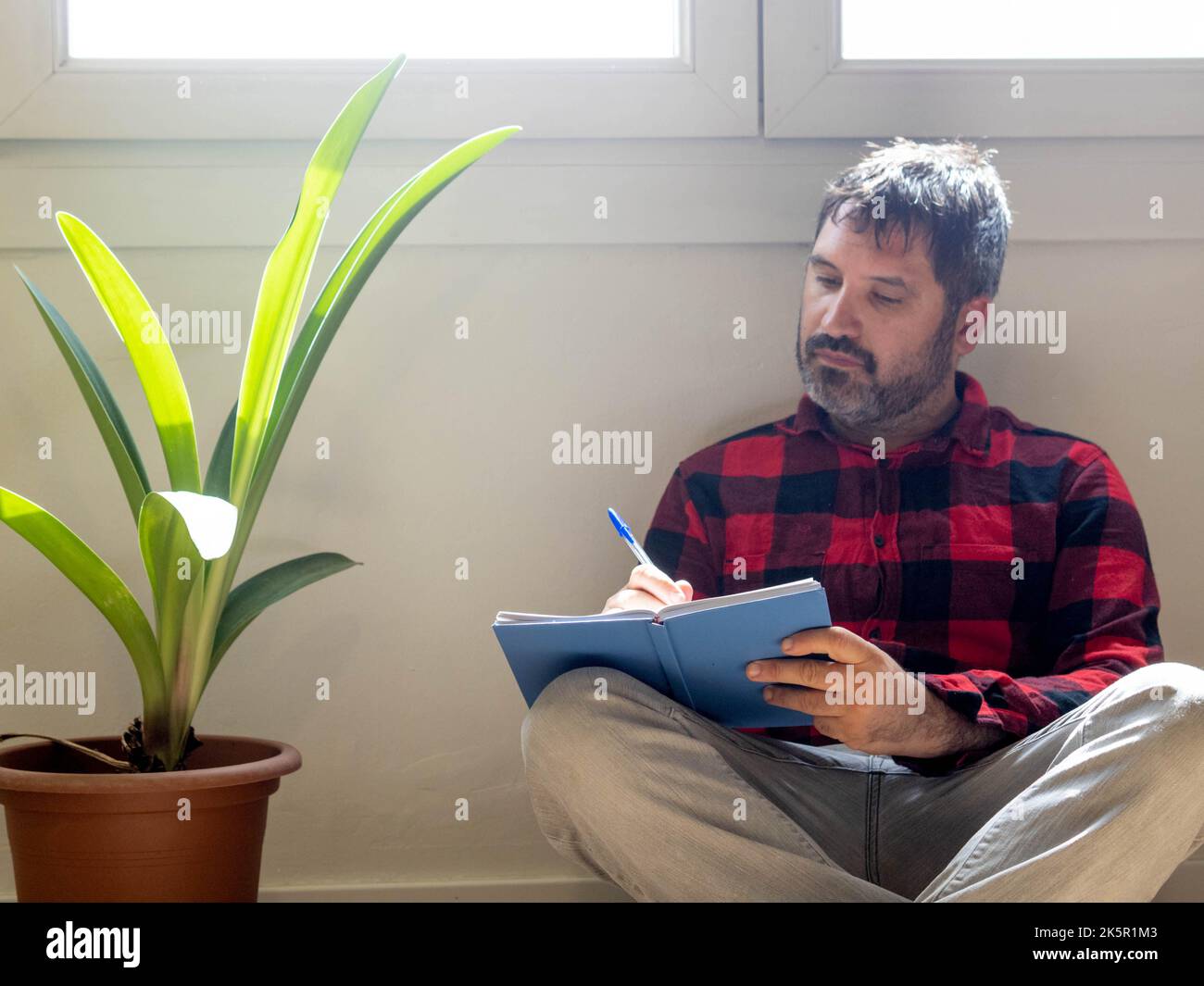 Hipster-Mann schreibt in einem Notizbuch in einer Wohnung Stockfoto