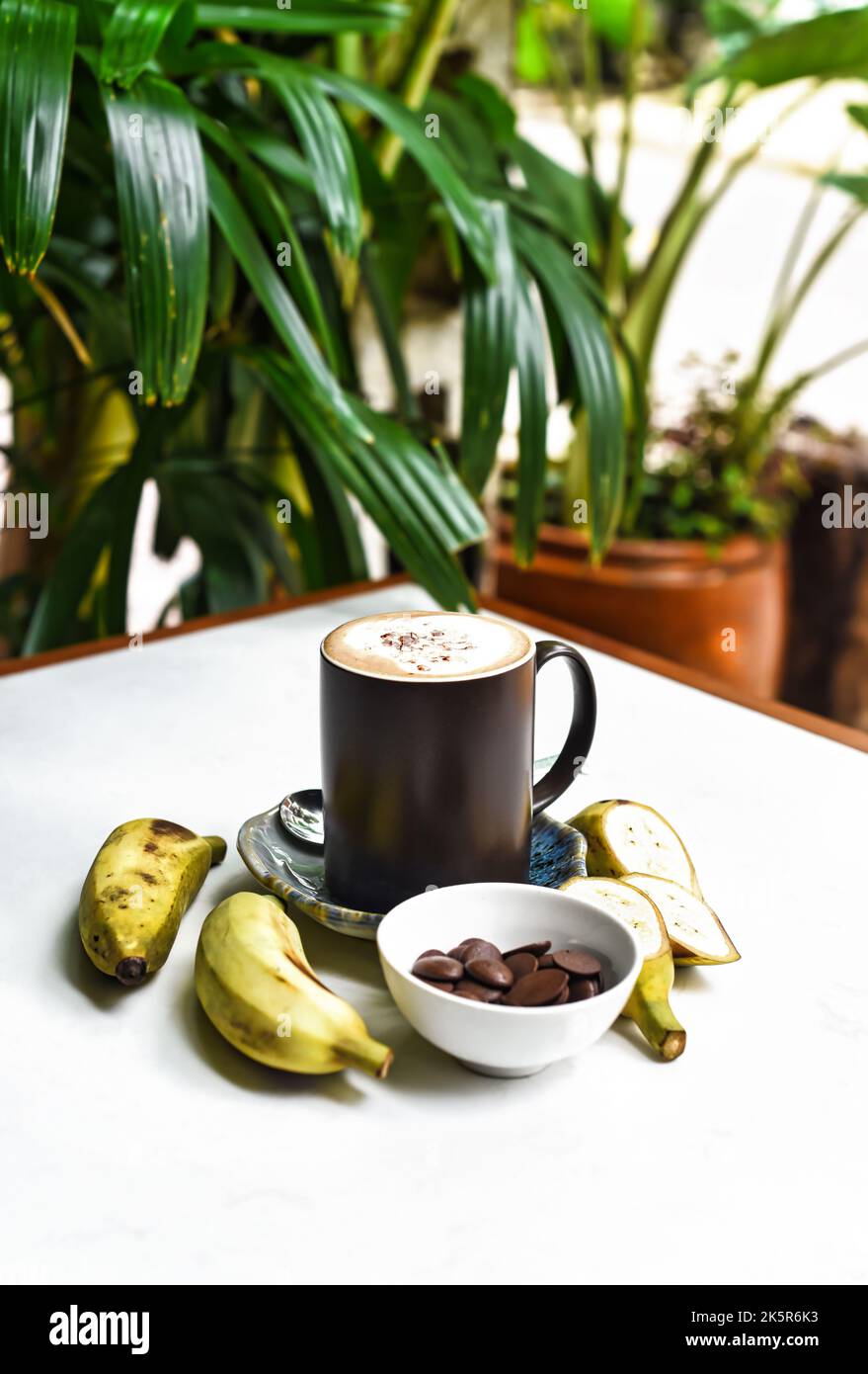 Bananenschokolade-Latte mit frischen Bananen- und Schokoladentropfen auf weißem Tisch Stockfoto