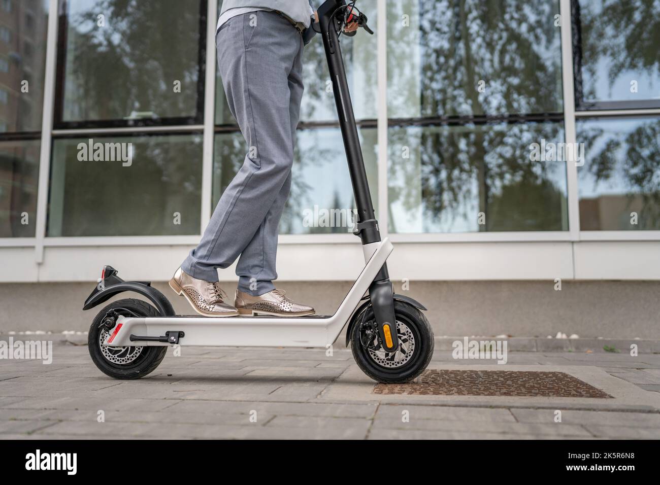 Füße von unbekannten Frau stehen oder fahren Elektro-Kick Scooter E-Scooter auf dem Bürgersteig am Tag umweltfreundliche moderne Transport in der Stadt oder Stadt Stockfoto